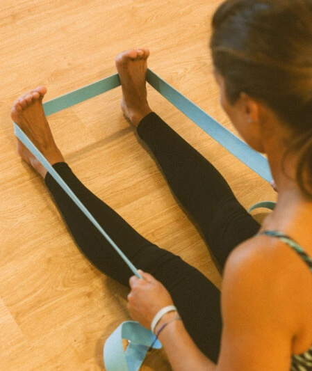 Postura de Pachimottanasana com ajuda de cinto de yoga, para alongamento e alívio de tensões profundas. Estúdio Yoga P em Milfontes